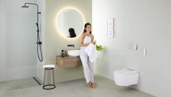 Mujer apoyada en un lavabo en un baño con inodoro bidé Sela, un lavabo y un mueble del baño Geberit VariForm.