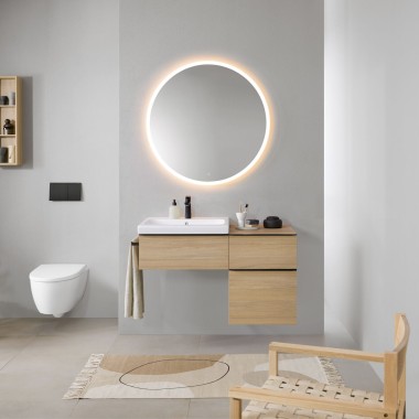 Baño con paredes grises, muebles de baño Geberit de madera y un espejo redondo con luz Geberit Option