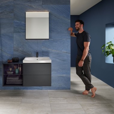 Hombre apoyado en la pared en un baño azul con lavabo Geberit Mix & Match Hombre apoyado en la pared en un baño azul con lavabo Geberit Mix & Match