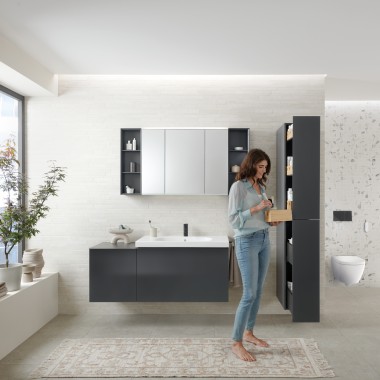 Una mujer abre un mueble alto Geberit Acanto con mucho espacio de almacenamiento Una mujer abre un mueble alto Geberit Acanto con mucho espacio de almacenamiento