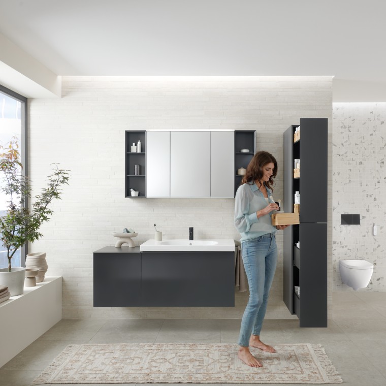 Una mujer abre un mueble alto Geberit Acanto con mucho espacio de almacenamiento Una mujer abre un mueble alto Geberit Acanto con mucho espacio de almacenamiento