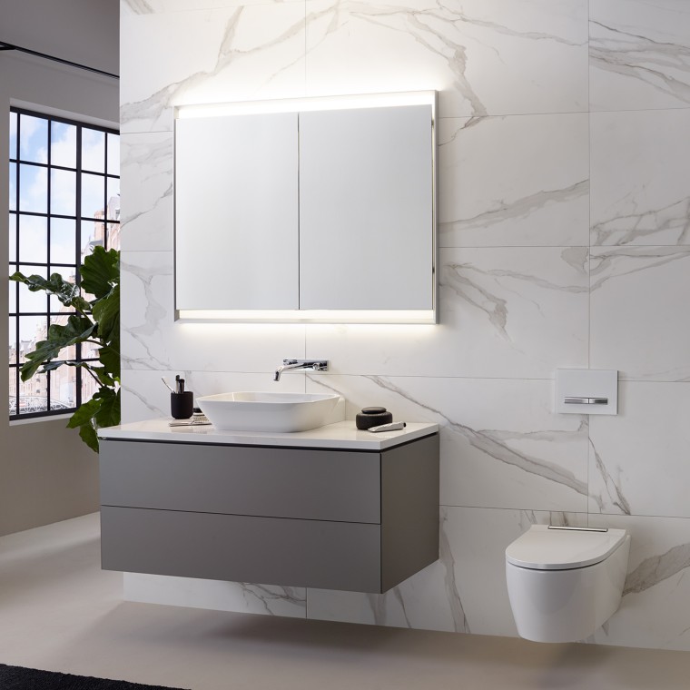 Baño con pared con baldosas con aspecto de mármol, lavabo y mueble Geberit ONE y armario con espejo con luz ComfortLight