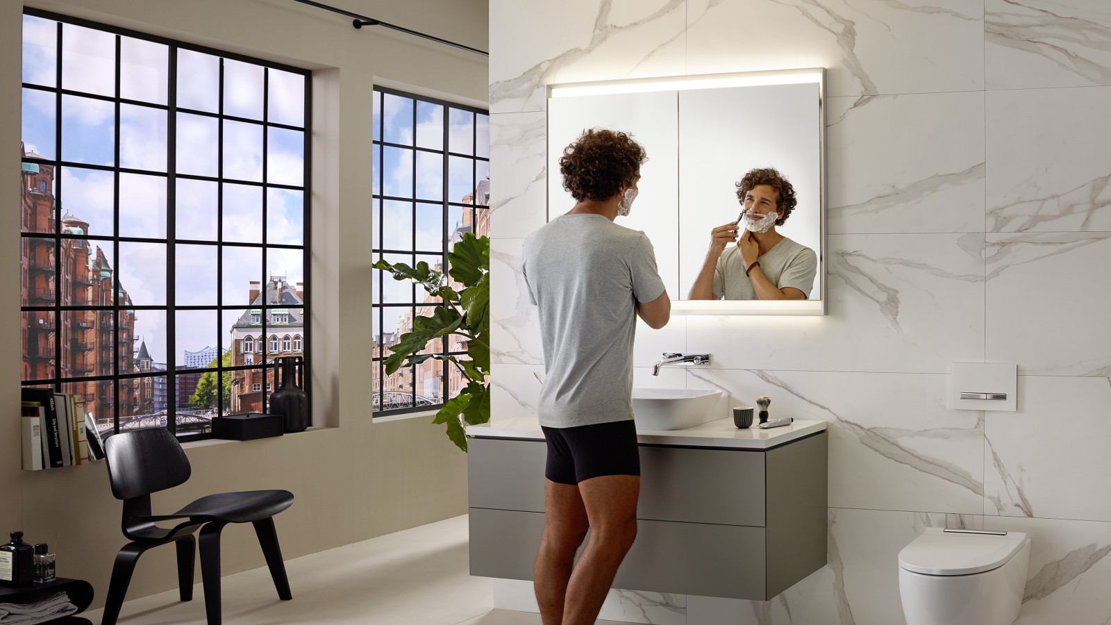 Hombre afeitándose en el lavabo con mueble y armario con espejo Geberit ONE Hombre afeitándose en el lavabo con mueble y armario con espejo Geberit ONE