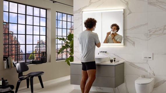 Hombre afeitándose en el lavabo con mueble y armario con espejo Geberit ONE