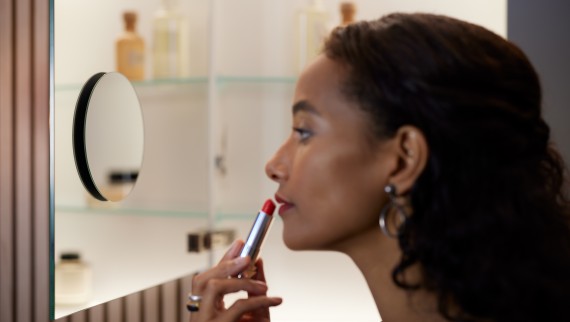 Mujer aplicándose lápiz labial frente a un espejo de aumento (© Geberit)