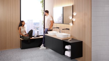 Mujer sentada en la ventana de un baño con productos Geberit ONE, hablando con un hombre Mujer sentada en la ventana de un baño con productos Geberit ONE, hablando con un hombre