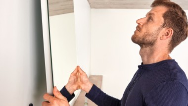 Hombre colgando un espejo Geberit Option durante la renovación de un baño