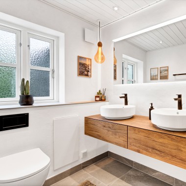 Baño renovado y luminoso con dos lavabos redondos, un gran espejo y muebles de baño de madera (© @triner2 y @strandparken3)
