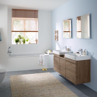 Baño familiar con pared azul celeste y muebles de baño en nogal hickory, espejos, pulsador y sanitarios Geberit