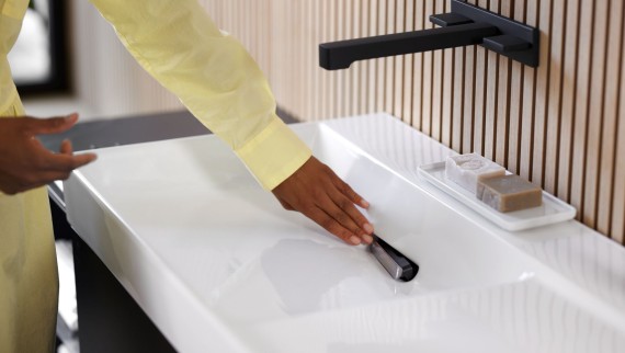 Mujer quita la tapa del desagüe con filtro anticabellos en el lavabo Geberit ONE con grifo en negro mate (© Geberit) Mujer quita la tapa del desagüe con filtro anticabellos en el lavabo Geberit ONE con grifo en negro mate (© Geberit)