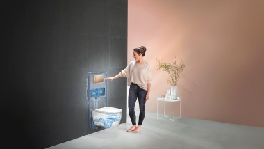 Mujer activando la descarga en la Solución Completa Geberit para el inodoro (© Geberit)