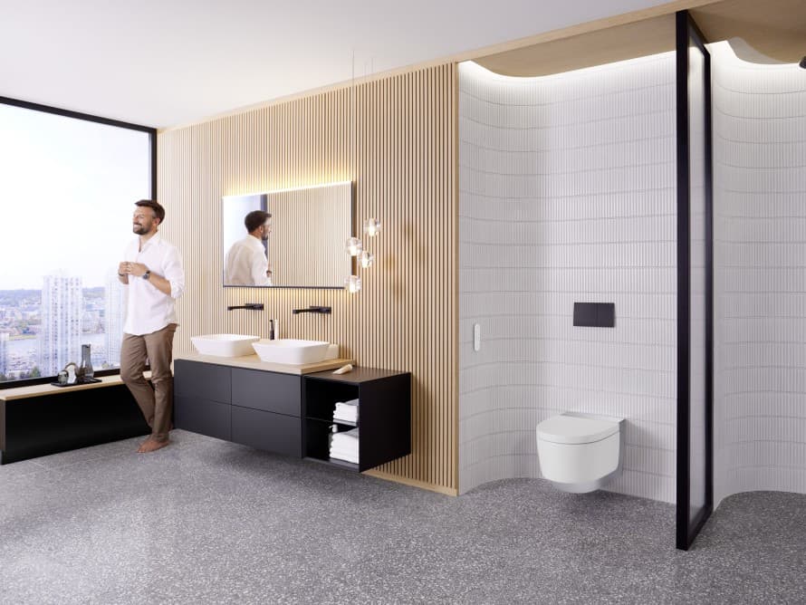 Hombre en un baño grande con muebles oscuros e inodoro bidé Geberit AquaClean Hombre en un baño grande con muebles oscuros e inodoro bidé Geberit AquaClean